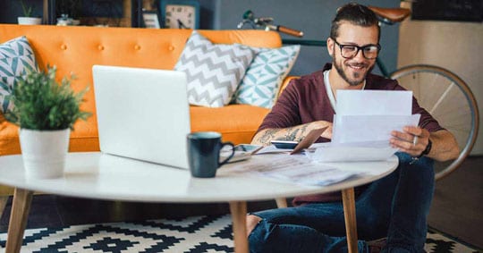 Man looking at papers with laptop open